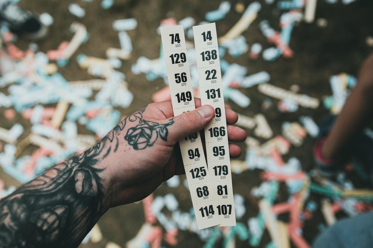 Close-up of a tattooed hand holding raffle tickets amidst confetti at a festival setting.