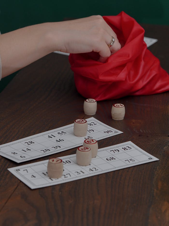 Hand reaching into red bag during wooden token bingo game on table.