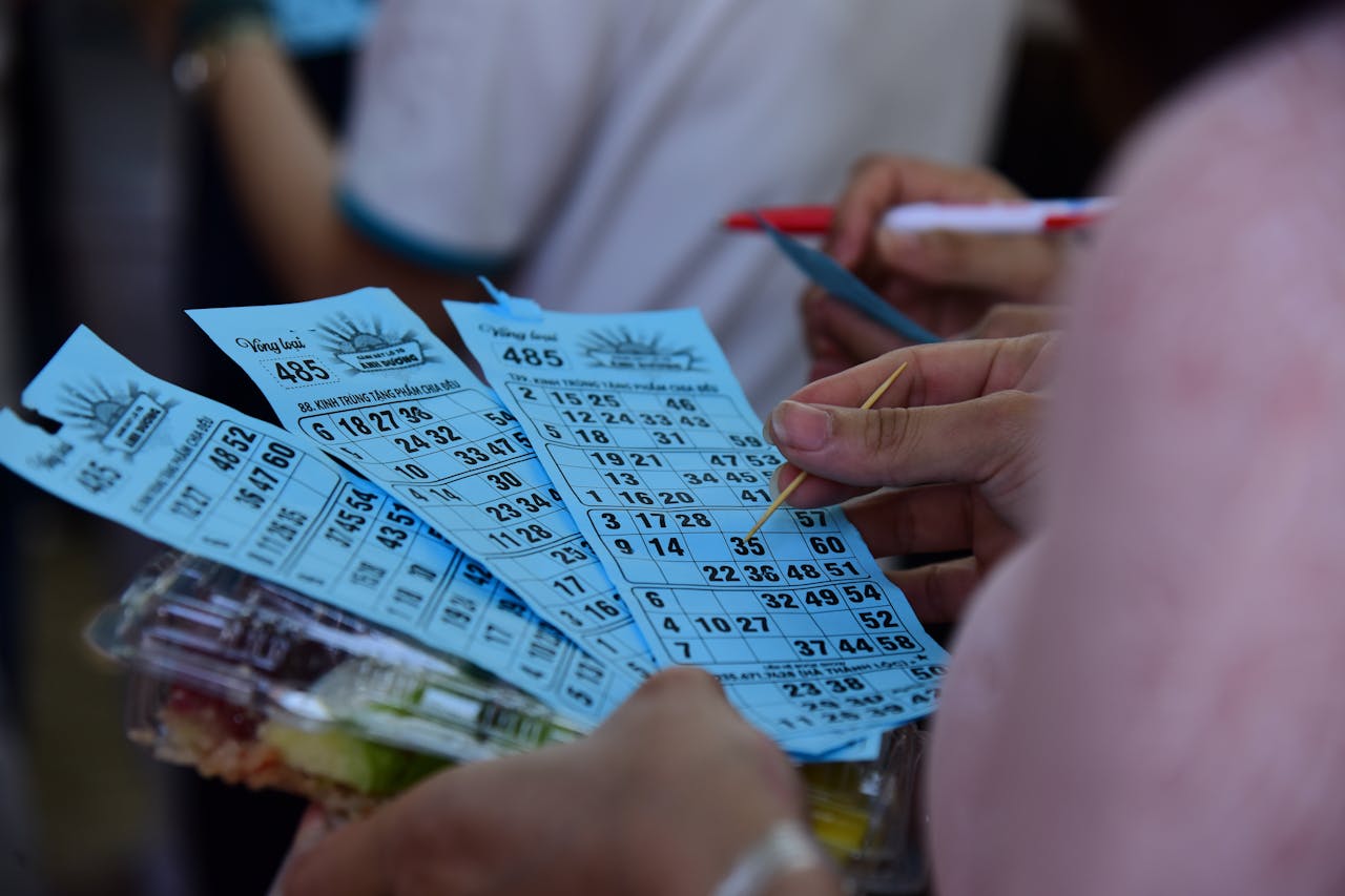 People playing bingo indoors, holding blue bingo cards with pen and markers.