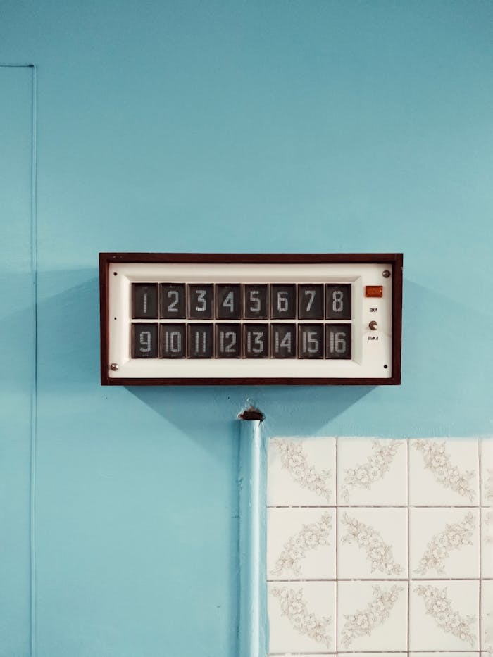 Retro wall clock displaying numbers on a blue tiled backdrop, perfect for decor inspiration.